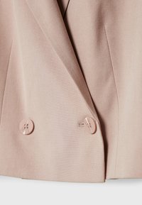 Light pink blazer with a smooth texture, featuring double-breasted front, two large round buttons, and sharp tailored lines.