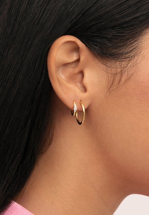 Pendientes de aro en tono dorado con un pequeño acento de diamante, que presentan un acabado pulido con una textura suave y forma circular.