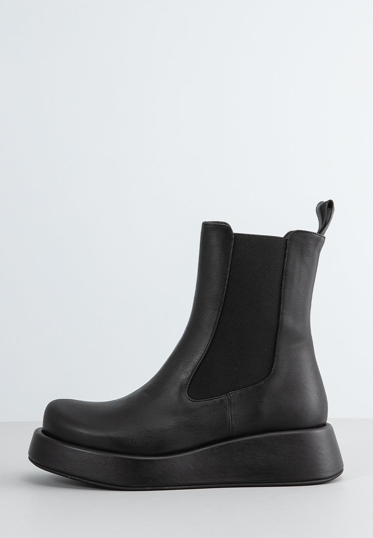 Botas negras de cuero hasta el tobillo con inserciones elásticas en los laterales y una suela de plataforma gruesa y elevada. Punta redondeada y tirador en el talón. Textura suave.