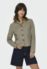 Ljusgrå mockajacka med krage, med rak passform och fem mörka knappar, kombinerad med mörka denimshorts.