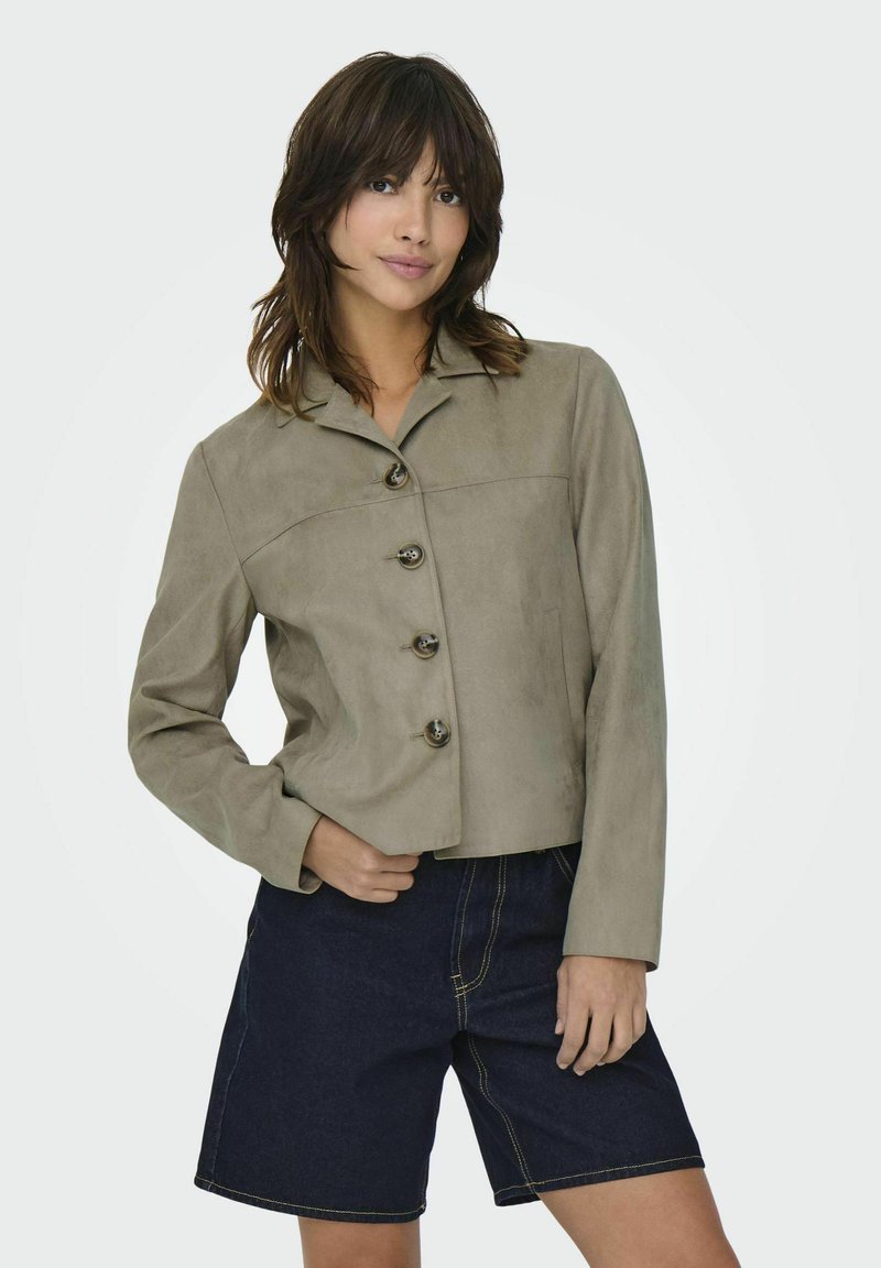 Ljusgrå mockajacka med krage, med rak passform och fem mörka knappar, kombinerad med mörka denimshorts.