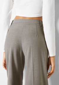 Grijze, op maat gemaakte broek met een gladde textuur, voorzien van een achterpijp en zijzakken, gecombineerd met een cropped wit top met lange mouwen.