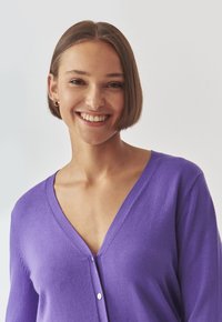 Purple, wool cardigan with a deep V-neck and a button closure. Soft texture and ribbed detailing along the edges.