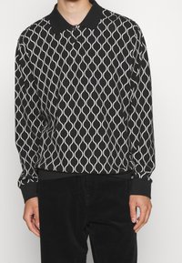 Polo à manches longues avec un motif ondulé noir et blanc, doté d'un col classique et de poignets côtelés aux manches et à l'ourlet.