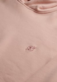 Sudadera rosa claro hecha de un tejido suave con un logo bordado en el pecho. Cuenta con capucha con cordones y puños acanalados.