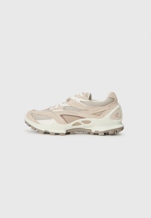 Zapatilla deportiva de color beige claro y crema con paneles de malla y ante, cierre de cordones y suela de goma resistente para uso al aire libre.