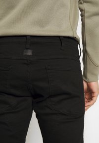 Svarta denimbyxor med slim fit, med detaljer av söm på bakfickorna och en subtil logotyp ovanför midjan.