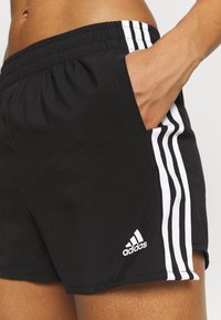 Pantalones cortos deportivos negros con cintura elástica, rayas blancas laterales y un logo de Adidas en el dobladillo. Incluyen bolsillos laterales.