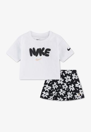 Biele krátke tričko s krátkym rukávom s čiernym nápisom "NIKE" a čierna sukňa s kvetinovým vzorom, obsahujúca biele logá a malé zlaté značky swoosh.