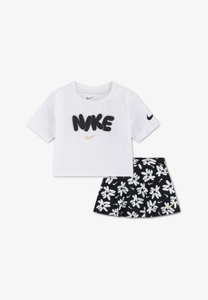 Hvit kortermet crop-top med svart "NIKE"-tekst og svart blomsterprintet skjørt med hvite logoer og små gullfargede swooshes.