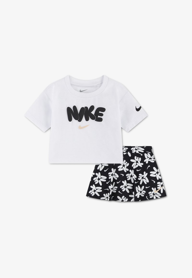 Haut court à manches courtes blanc avec texte "NIKE" en noir et jupe à motif floral noir comportant des logos blancs et de petites virgules dorées.
