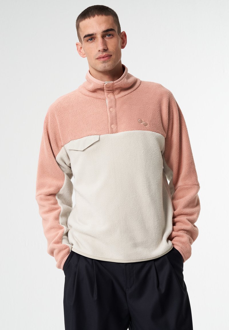 Fleece-Pullover in Rosa und Creme, mit hohem Kragen, Knopfleiste und einer Brusttasche. Weicher Stoff mit kontrastierenden Farben.