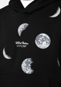 Haut à capuche noir avec des motifs en forme de croissant et de pleine lune brodés en argent, avec le texte du logo centré en dessous des motifs. Texture douce.