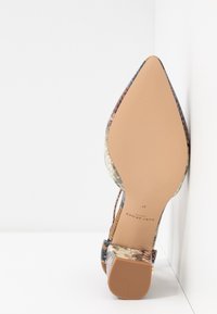 Chaussure à talon haut à bout pointu avec semelle beige et motif peau de serpent, vue de dessous contre un coin blanc.