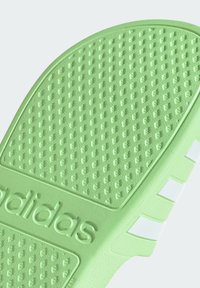 Zeleni gumeni potplat s teksturiranim uzorkom za grip, s reljefnim logotipom "adidas" i bijelim naglasnim prugama duž strane.