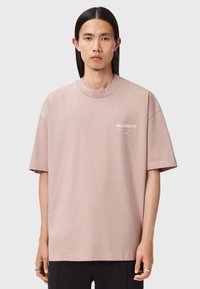 Helles, rosa Baumwoll-T-Shirt mit Rundhalsausschnitt, kurzen Ärmeln und lässiger Passform. Mit einem kleinen weißen Logo auf der Brust.