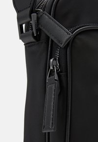 Sac à épaule en nylon noir avec une surface texturée, doté d'une fermeture éclair et d'accents en métal. Logo signature sur la bandoulière. Design compact.