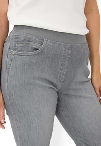 Jean stretch gris avec une taille élastique douce, doté d'une poche avant et d'une finition en denim texturé. Détails de couture minimaliste sur le côté.