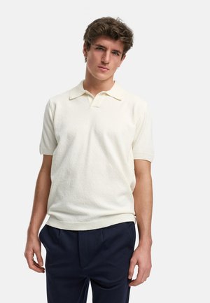 Kortærmet polo skjorte i off-white strikket stof med en struktureret overflade. Har en klassisk krave og ribbede manchetter, parret med marineblå bukser.
