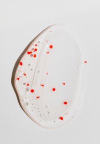 Klar geléagtig substans med en glat, blank overflade, med små røde og pink prikker, placeret på en hvid overflade.