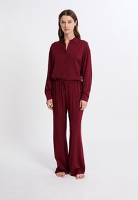 Bordeaux lounge set bestaande uit een knoopsluiting overhemd met lange mouwen en wijde broek met een verstelbare tailleband, gemaakt van zachte, vloeiende stof.