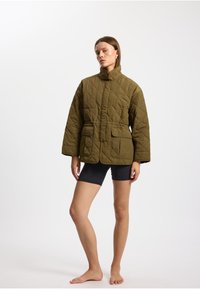 Geplüschte olivgrüne Jacke mit hohem Kragen, zwei Vorderaschen und geradem Schnitt. Der Stoff hat eine glatte, matte Textur.