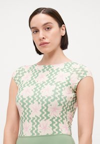 Haut vert à manches courtes avec un motif floral en rose et crème sur un fond ondulé. Coupe ajustée et texture lisse.