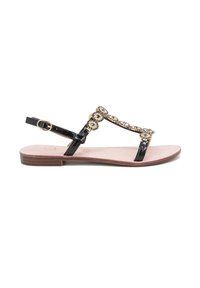 Sandalo in pelle verniciata nera con suola piatta, dotato di una tracolla decorativa di pietre circolari e di una chiusura con fibbia alla caviglia.