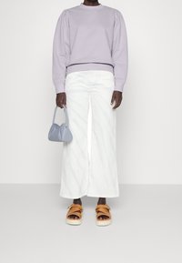 Ljus lavendelfärgad sweatshirt med puffärmar, vita vida byxor, ljusblå handväska och bruna plattformssandaler. Minimalistisk design och texturer.