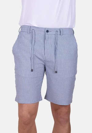 Persona con pantalones cortos de rayas verticales azules y blancas con cordón y camisa blanca, mostrada de la cintura hasta justo por encima de las rodillas.