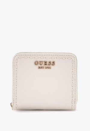 Portafoglio in pelle beige con bordi cuciti, logo dorato "GUESS EST. 1981" sul fronte, chiusura con zip, forma quadrata compatta.