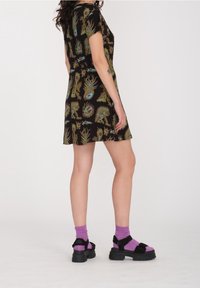 Robe noire à motifs avec des designs floraux et animaliers colorés, associée à des sandales à plateforme noires et des chaussettes violettes. Manches courtes, coupe décontractée.