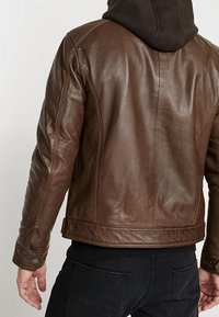 Brun læderjakke med en glat tekstur, der har et tætsiddende design og syninger som detalje. Indeholder en sort hættetrøje under.