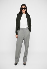 Πράσινο φούτερ με φερμουάρ, λευκό πουκάμισο και γκρίζες παντελόνες με ψηλή μέση. Μαύρα γωνιώδη γυαλιά ηλίου και μυτερές μαύρες γόβες ολοκληρώνουν το σύνολο.