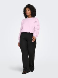 Light pink sweatshirt with floral cut-out details on sleeves, paired with black straight-leg pants and black flats. Model stands upright.