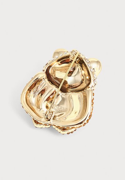 Broche ourson couleur or avec des accents en strass sur les oreilles et une attache épingle à l'arrière pour fixer.