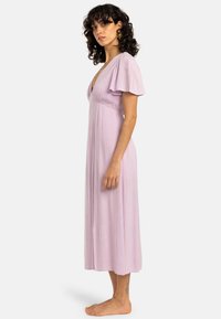 Light purple midi dress with short flutter sleeves, a deep V-neck, and a flowing, textured fabric. Barefoot model stands in profile.