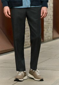 Mørkegrå skræddersyede bukser med en glat tekstur, parret med beige sneakers med hvide snørebånd og en kraftig sål.