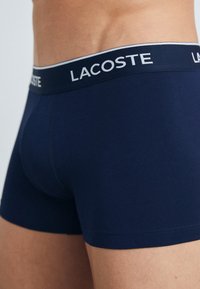 Boxers en coton bleu marine avec une ceinture tissée blanche et bleu marine portant le logo "LACOSTE". Texture douce et design ajusté.