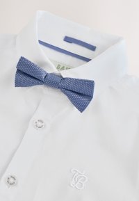 Chemise blanche habillée avec logo brodé "TB" et nœud papillon bleu à motifs sur le col, boutons marqués "Ted Baker".
