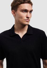 Polo shirt nera realizzata in tessuto strutturato, con colletto a V corto e maniche corte. Design minimalista senza motivi visibili.