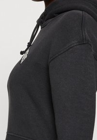 Czarna bluza z kapturem wykonana z miękkiego materiału, z regulowanym kapturem, ściągaczami przy rękawach oraz dyskretnym logo w okolicy dekoltu.