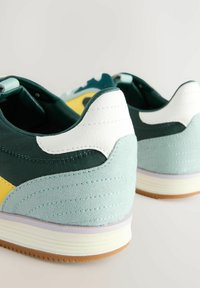 Sneaker con una toma superiore verde scuro, morbidi accenti blu chiaro, linguetta sul tallone bianca e dettaglio giallo. Il camoscio testurizzato e la suola in gomma offrono grip.
