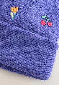 Bonnet tricoté violet avec une texture côtelée. Présente une tulipe jaune brodée et des cerises rouges à l'avant. Matière douce et extensible.