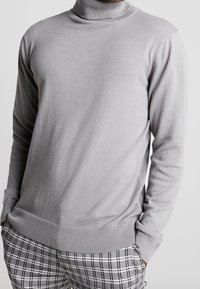 Grå polotröja med långa ärmar, ribbade manschetter och nederkant, tillverkad av ett mjukt, lätt material, kombinerad med rutiga byxor.