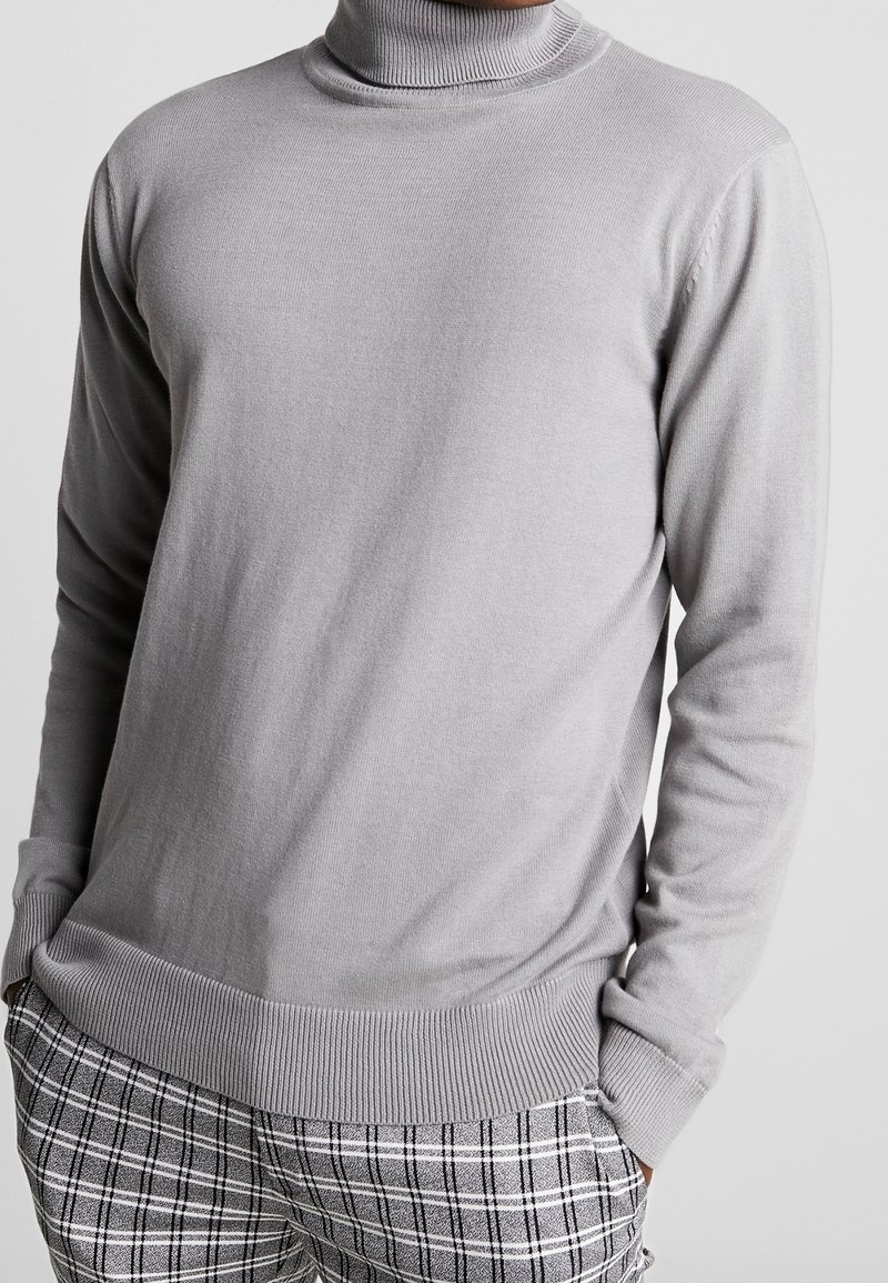 Grå polotröja med långa ärmar, ribbade manschetter och nederkant, tillverkad av ett mjukt, lätt material, kombinerad med rutiga byxor.