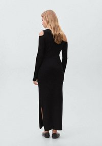 Abito nero in maglia con maniche lunghe, dettagli cut-out sulle spalle e spacco laterale. Presenta una silhouette aderente e una texture morbida.