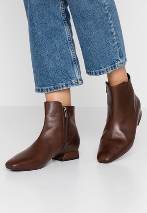 Bottes basses en cuir marron avec un bout pointu et un petit talon bloc, dotées d'une fermeture éclair latérale et d'une texture lisse. Portées avec un jean raccourci.