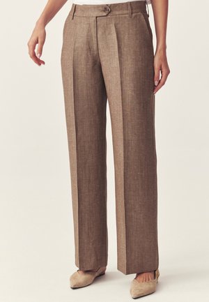 Hnedé široké nohavice s vysokým pásom, s prednými záhybmi, zapínaním na gombík a pútkami na opasok, nosené s béžovými špicatými balerínami.