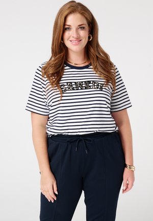 Gestreept T-shirt met korte mouwen in marineblauw en wit met pailletten tekst; gecombineerd met joggingsbroek met elastische tailleband in donkere kleur.